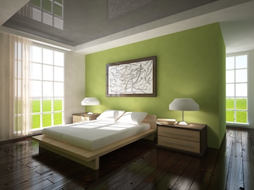 room with a hardwood floor, bright windows on two sides, and a two-person bed with a beside table and lamp on eachside